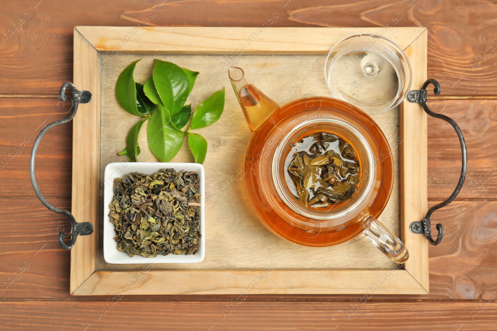 Photo of Wooden tray with hot aromatic tea, dry and fresh leaves on wooden table, top view