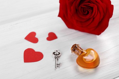 Photo of Heart shaped bottlelove potion with small key, paper hearts and red rose flower on white wooden table