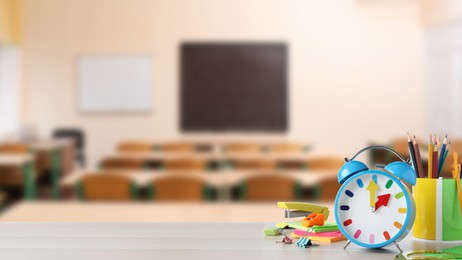 Image of Light blue alarm clock and different stationery on wooden table in classroom, space for text