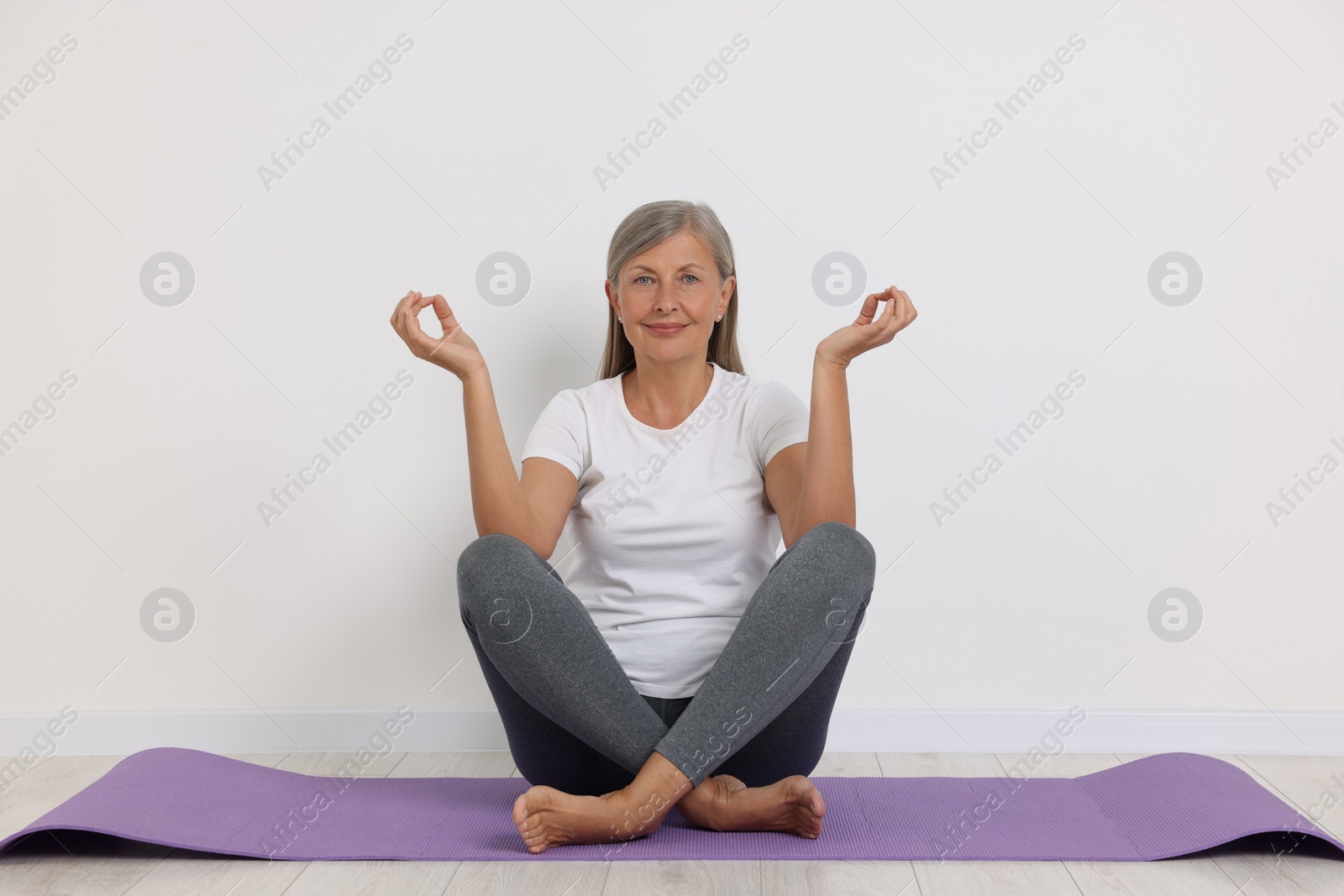 Photo of Happy senior woman practicing yoga on mat near white wall