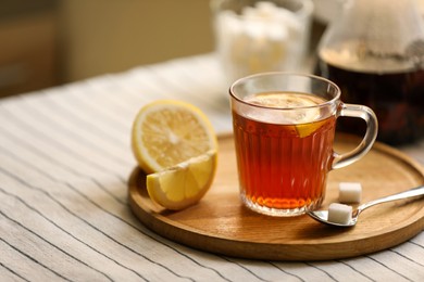 Photo of Glass mug of aromatic tea with lemon and sugar on table. Space for text