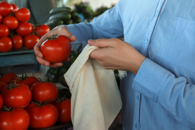 Woman putting tomato into cotton eco bag at wholesale market, closeup. Life without plastic