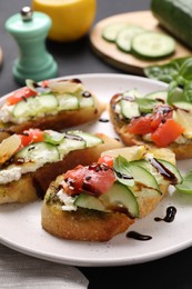 Photo of Delicious bruschettas with balsamic vinegar and toppings on black table