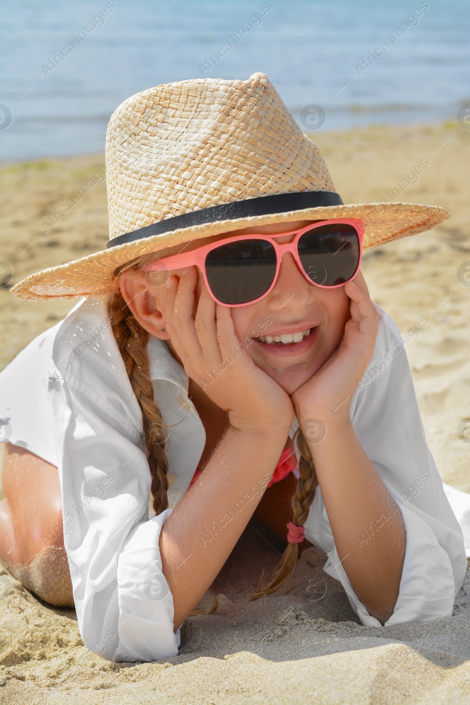 Photo of Little girl wearing sunglasses and hat at beach on sunny day