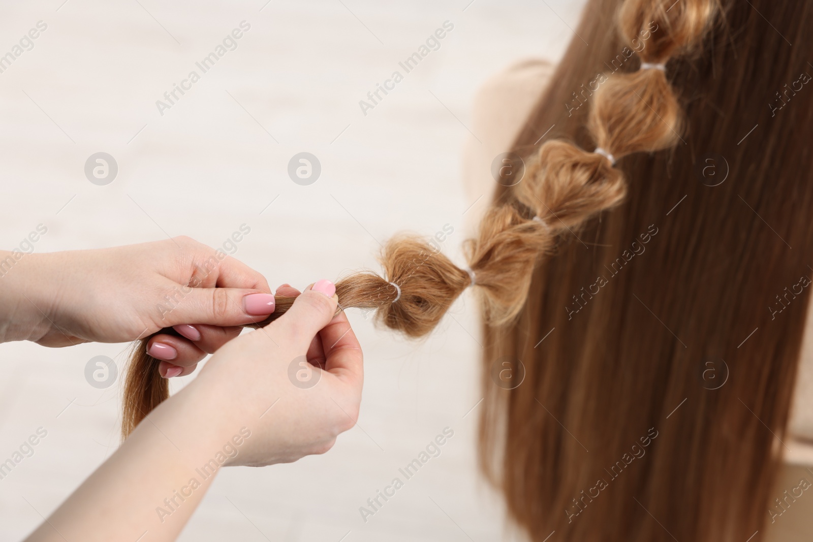 Photo of Professional stylist braiding woman's hair on blurred background, closeup