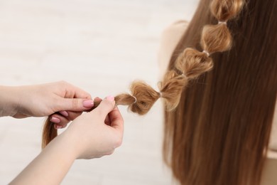 Professional stylist braiding woman's hair on blurred background, closeup