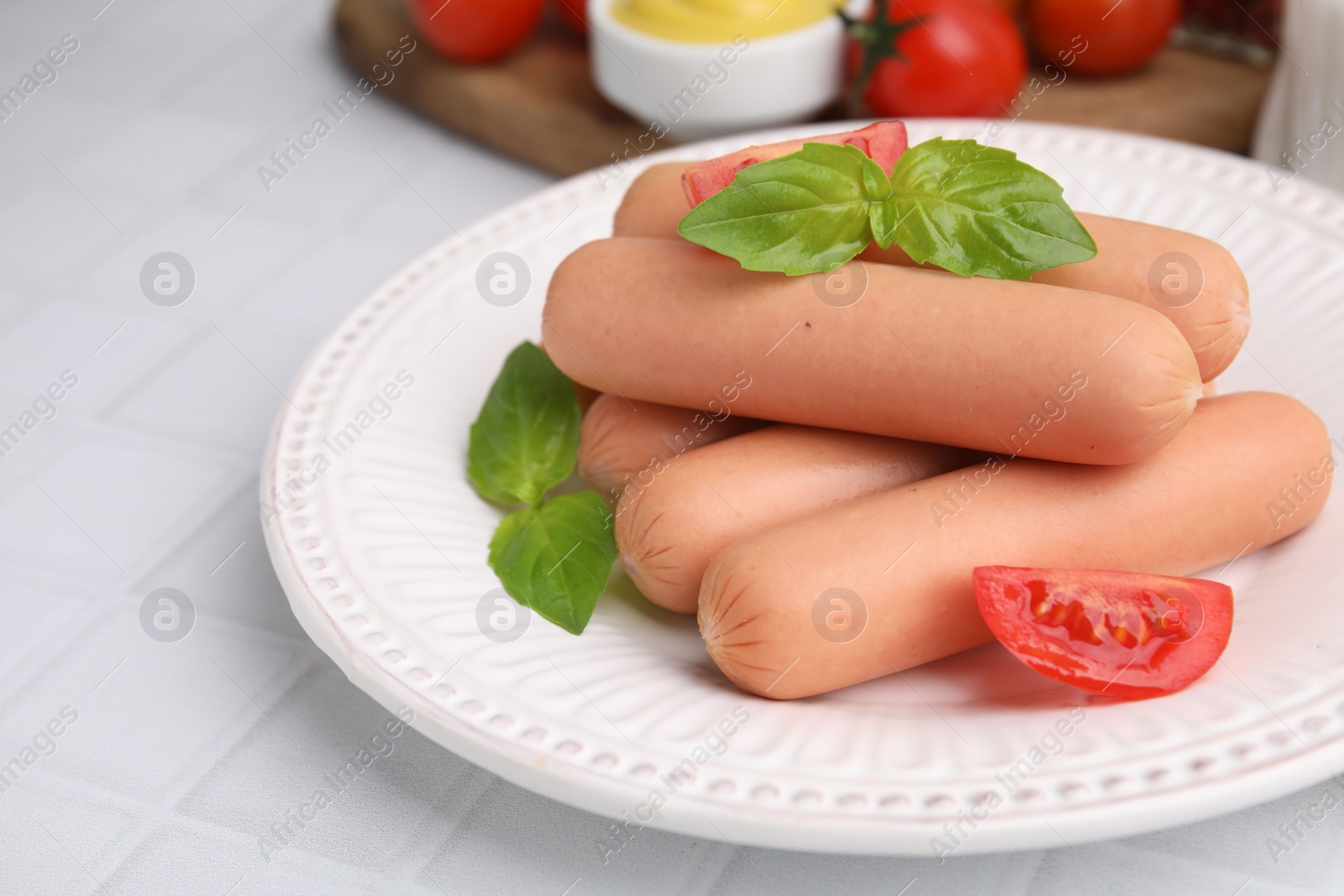 Photo of Delicious boiled sausages, tomatoes and basil on white tiled table, closeup