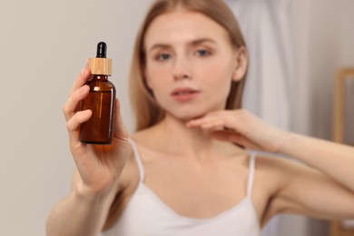 Photo of Woman with bottle of essential oil indoors, selective focus. Space for text