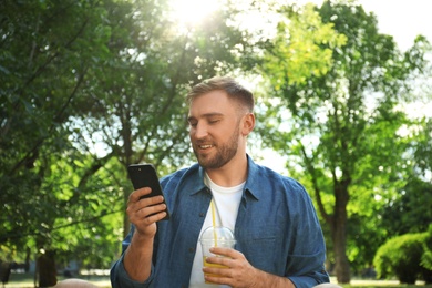 Photo of Young man with refreshing drink and smartphone in park