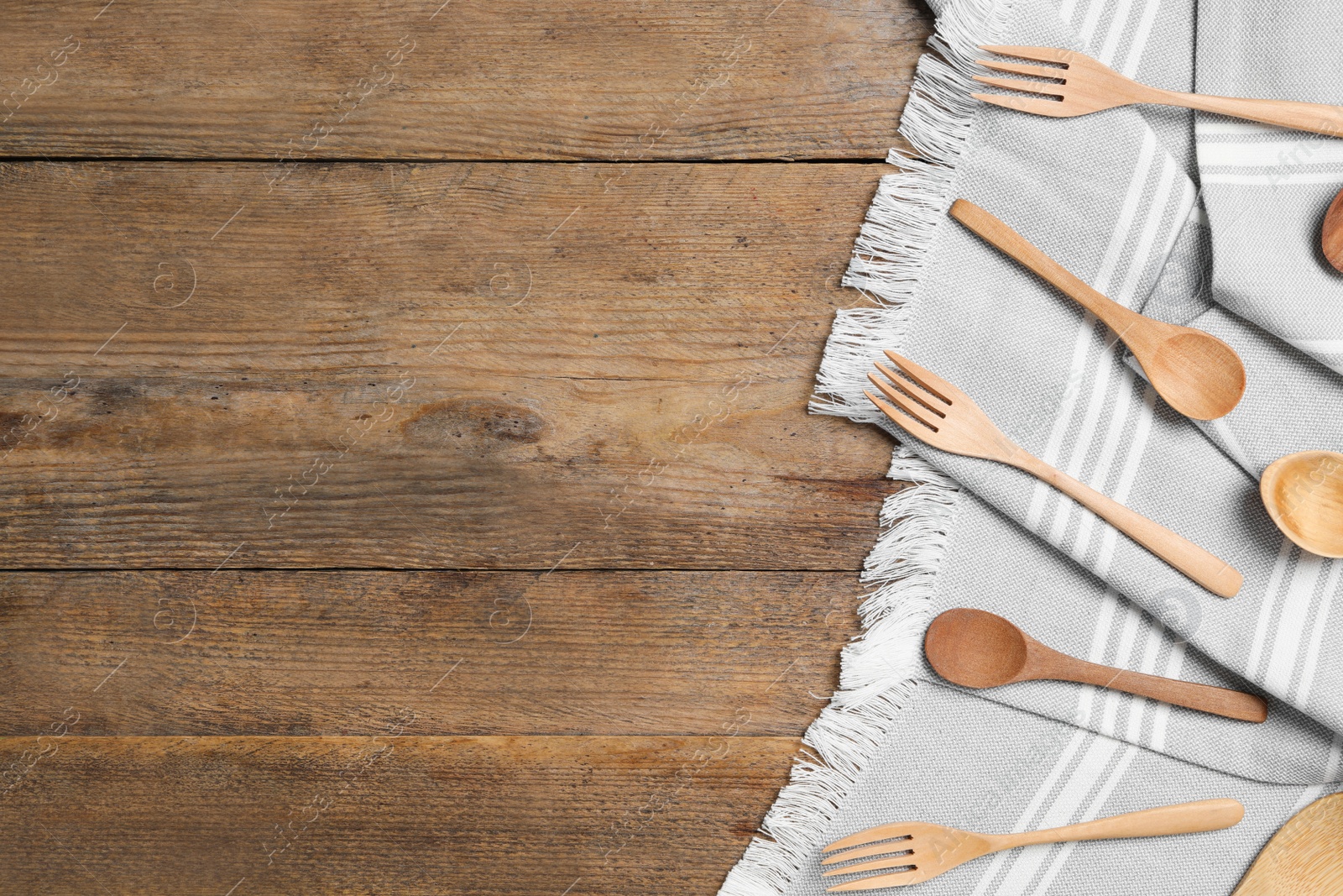 Photo of Grey cloth, spoons and forks on wooden table, flat lay with space for text. Cooking utensils