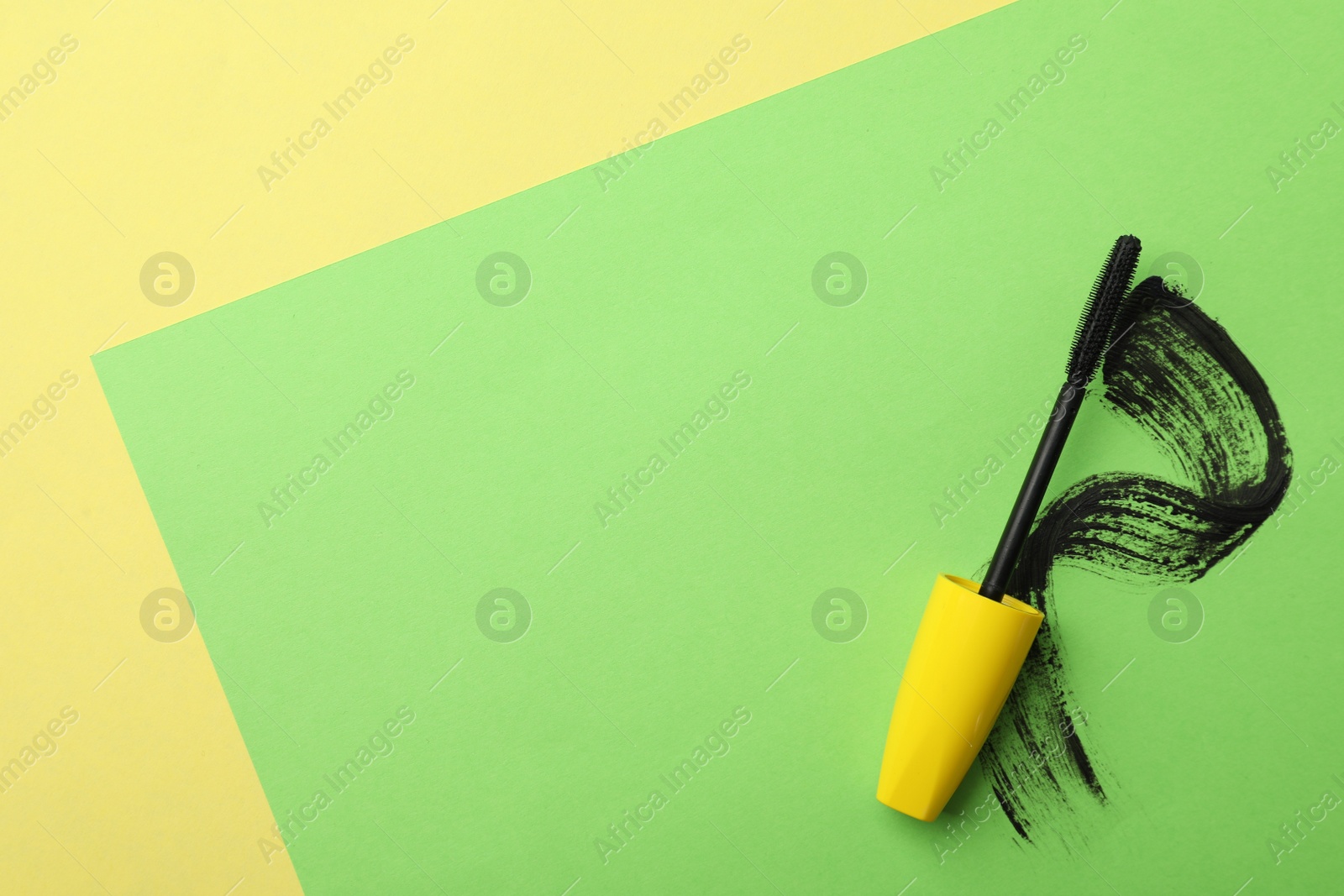 Photo of Mascara wand and smear on color background, top view with space for text. Makeup product