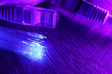 Photo of Optical fiber strands transmitting color light and cable with modular connectors on table, closeup. Space for text