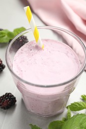 Photo of Delicious blackberry smoothie in glass with straw on white table, closeup