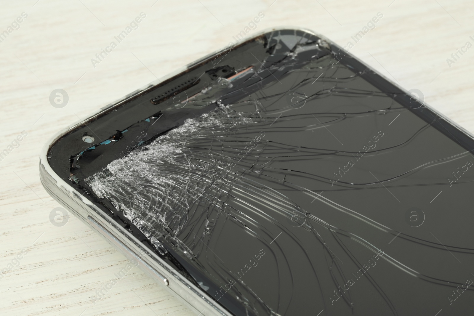 Photo of Smartphone with cracked screen on light beige wooden background, closeup. Device repair