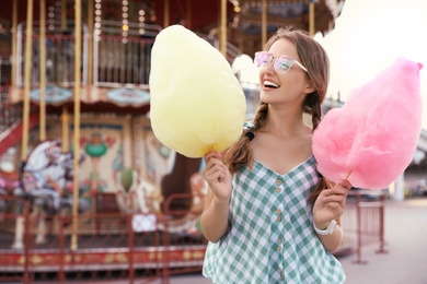 Young woman with cotton candies in amusement park. Space for text