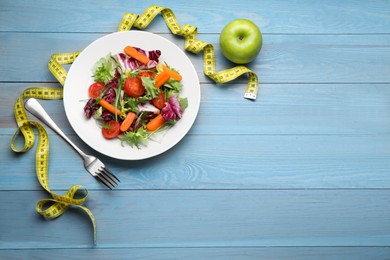 Photo of Plate of fresh vegetable salad, apple and measuring tape on light blue wooden table, flat lay with space for text. Healthy diet concept