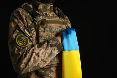 Soldier in military uniform with Ukrainian flag on black background, closeup