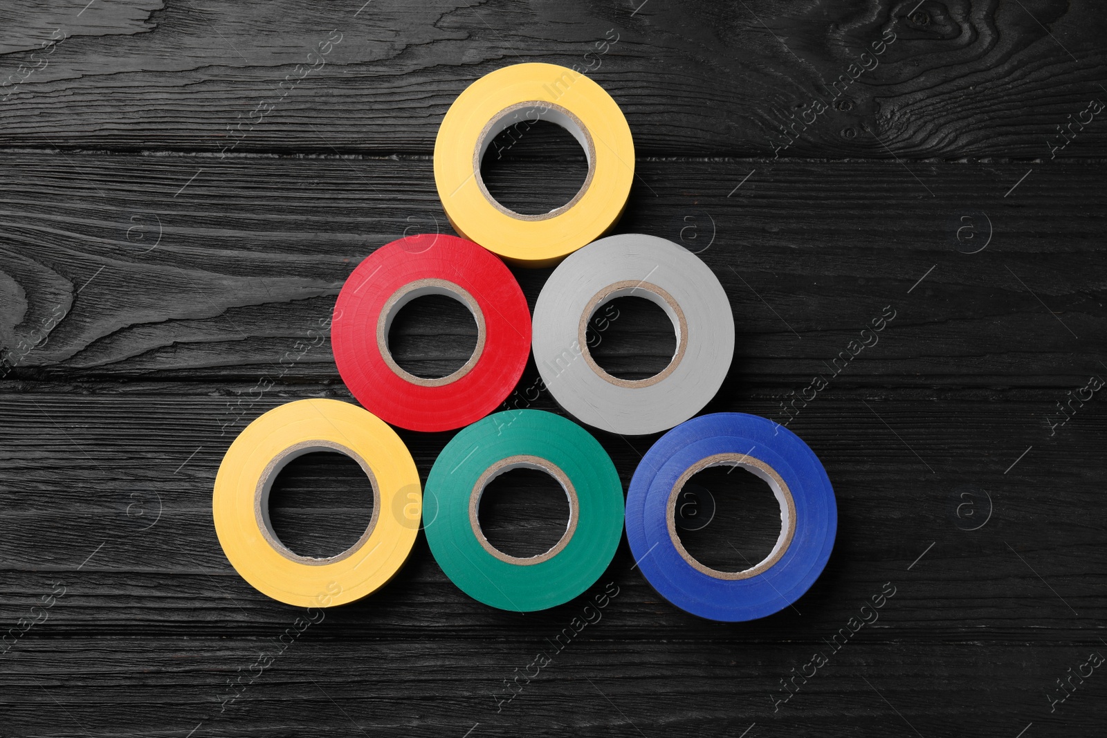 Photo of Colorful insulating tapes on black wooden table, flat lay