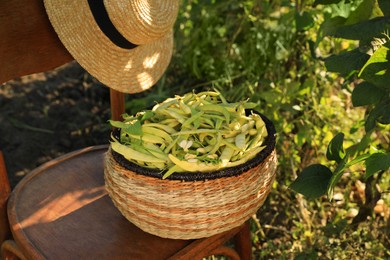 Photo of Wicker basket with fresh green beans and hat on wooden chair in garden