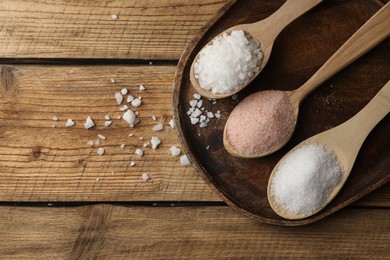 Photo of Different natural salt in spoons on wooden table, flat lay. Space for text