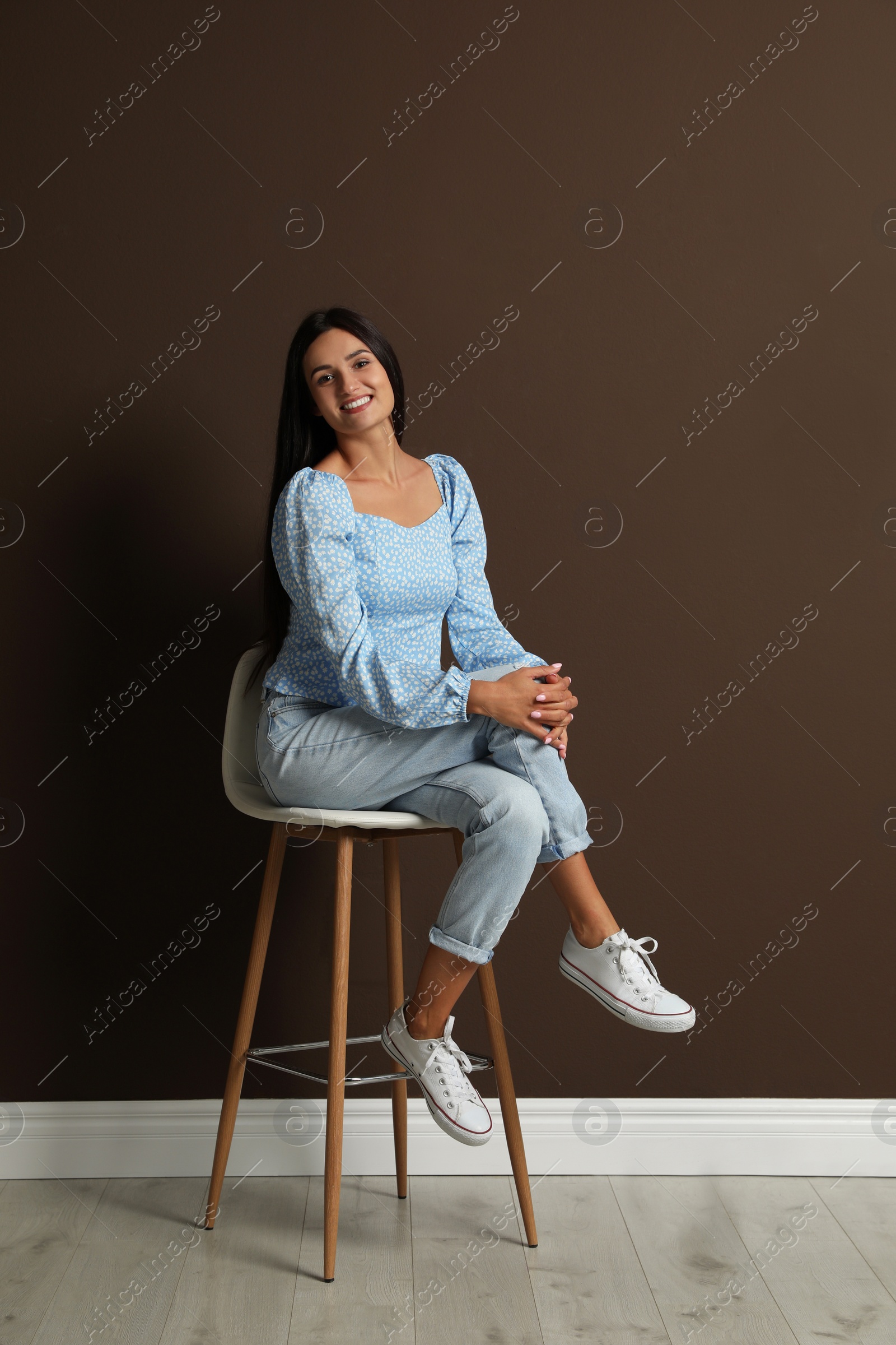 Photo of Beautiful young woman sitting on stool near brown wall