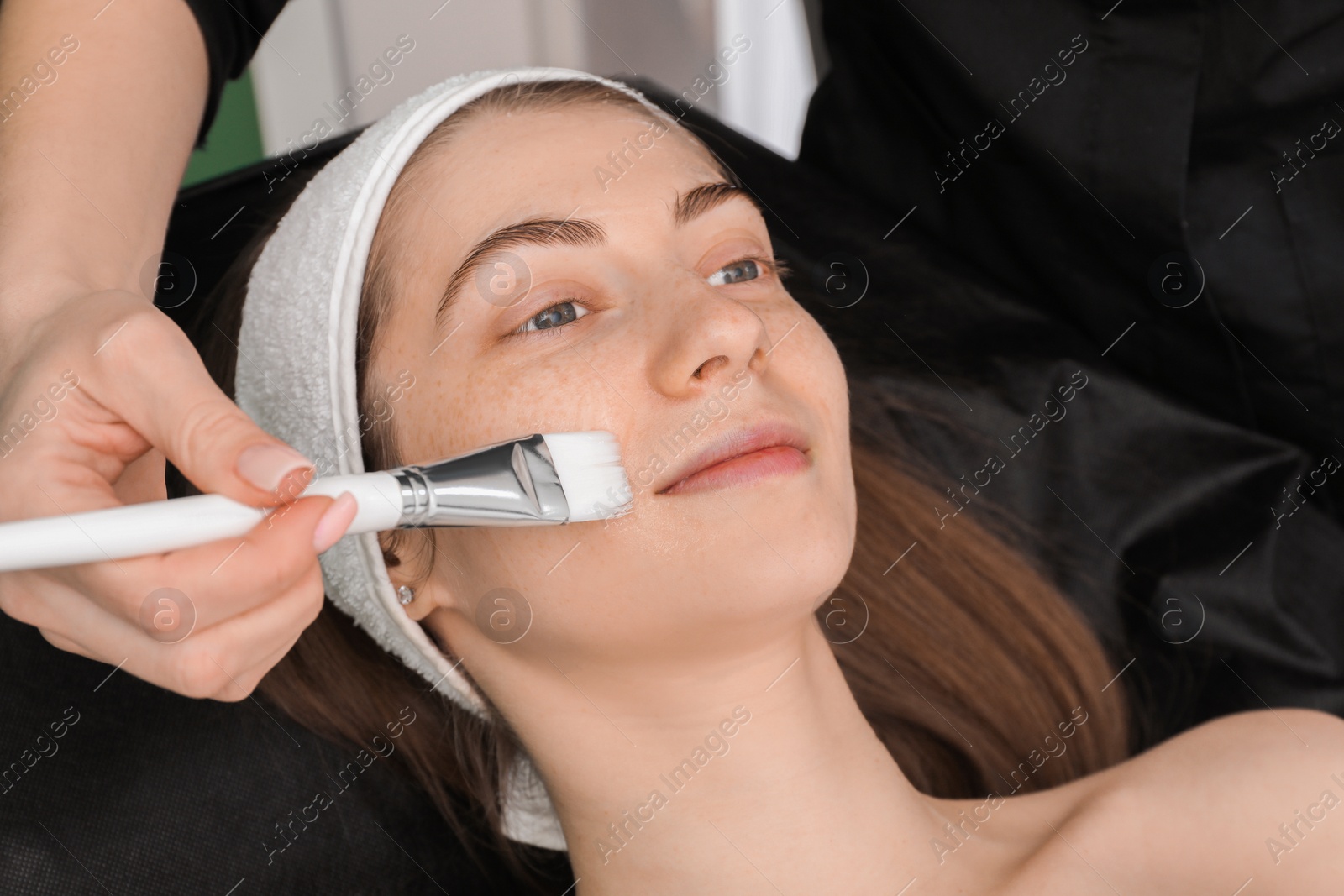 Photo of Cosmetologist applying mask on woman's face in clinic, closeup