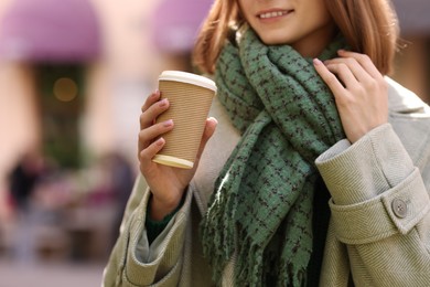 Photo of Beautiful woman in warm scarf with paper cup of coffee on city street, closeup. Space for text