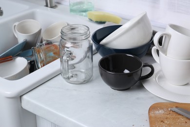 Many dirty utensils and dishware on countertop in messy kitchen