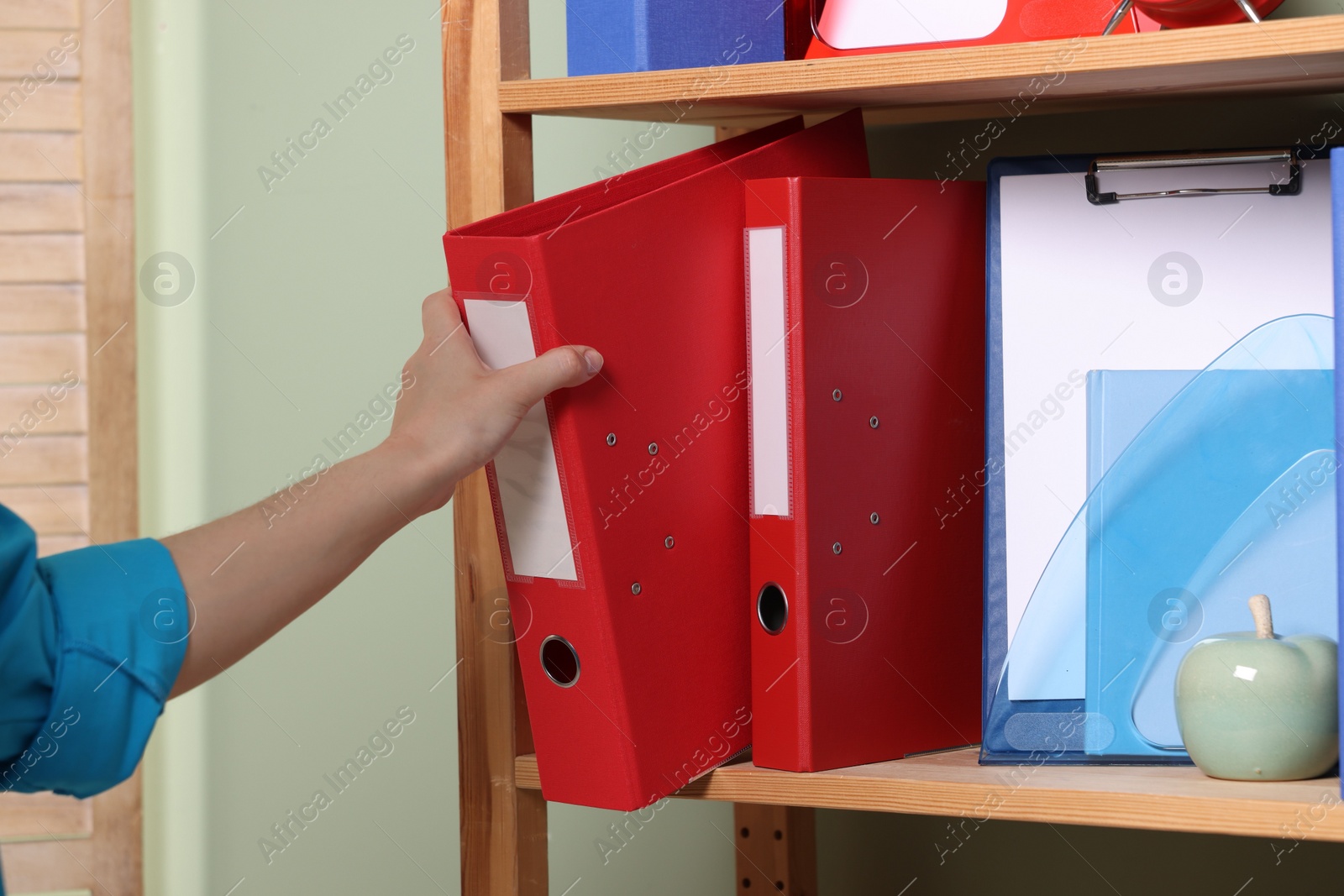 Photo of Woman taking binder office folder from shelving unit indoors, closeup