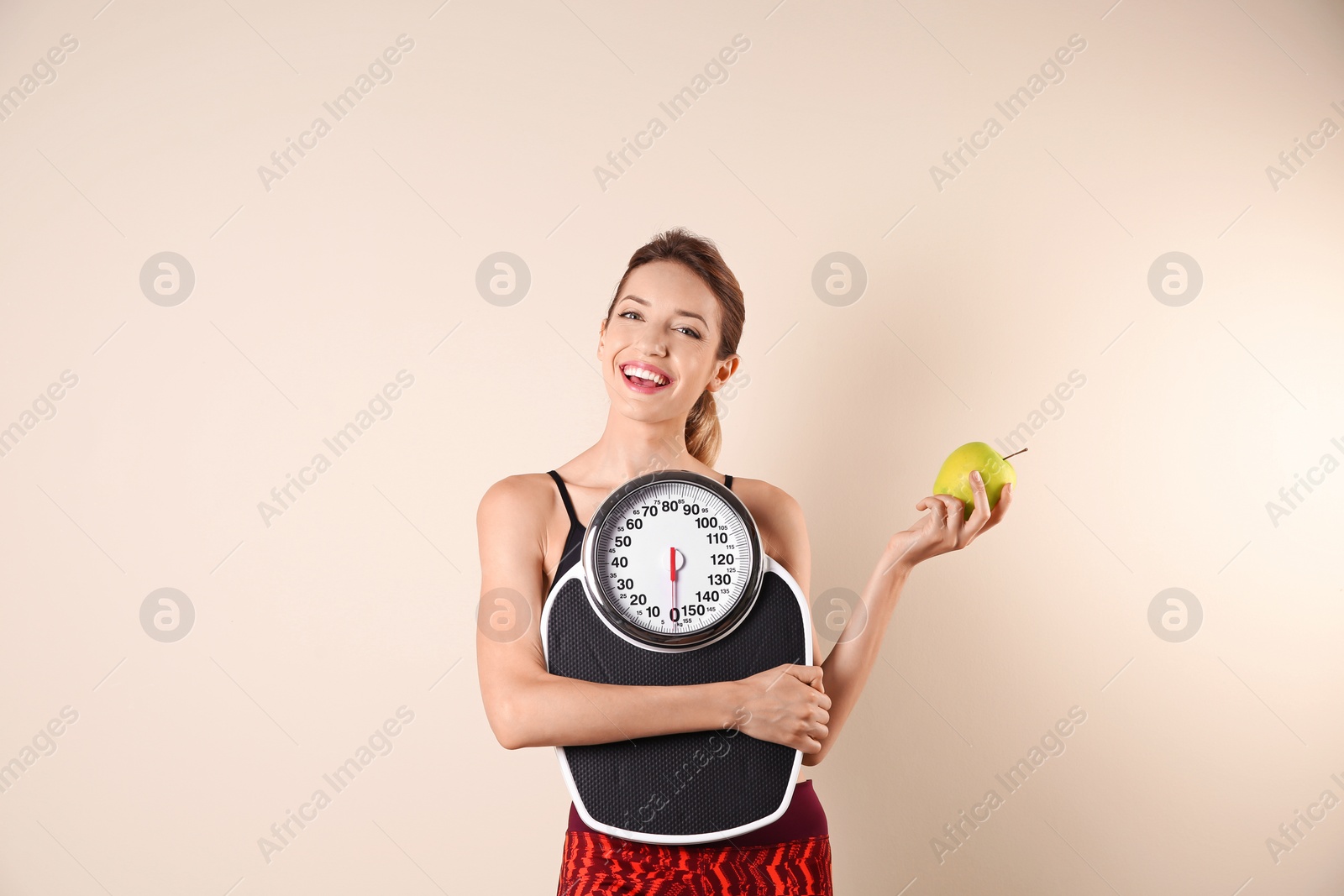 Photo of Young beautiful woman with scales and apple on light background. Weight loss motivation