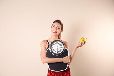 Photo of Young beautiful woman with scales and apple on light background. Weight loss motivation