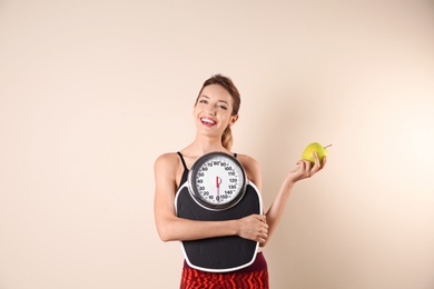 Young beautiful woman with scales and apple on light background. Weight loss motivation