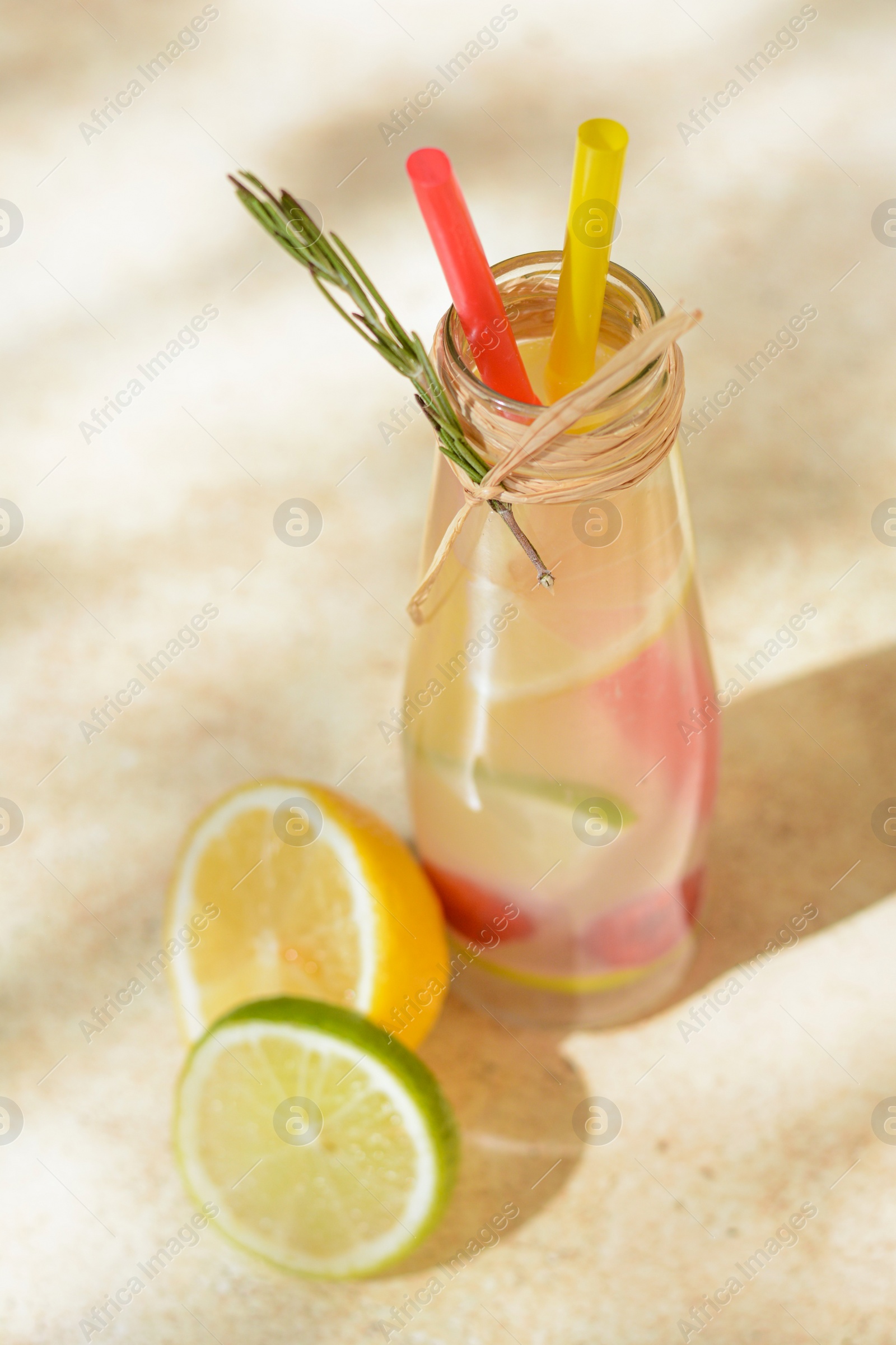 Photo of Refreshing tasty lemonade served in glass bottle and citrus fruits on beige table, above view