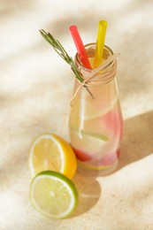 Photo of Refreshing tasty lemonade served in glass bottle and citrus fruits on beige table, above view