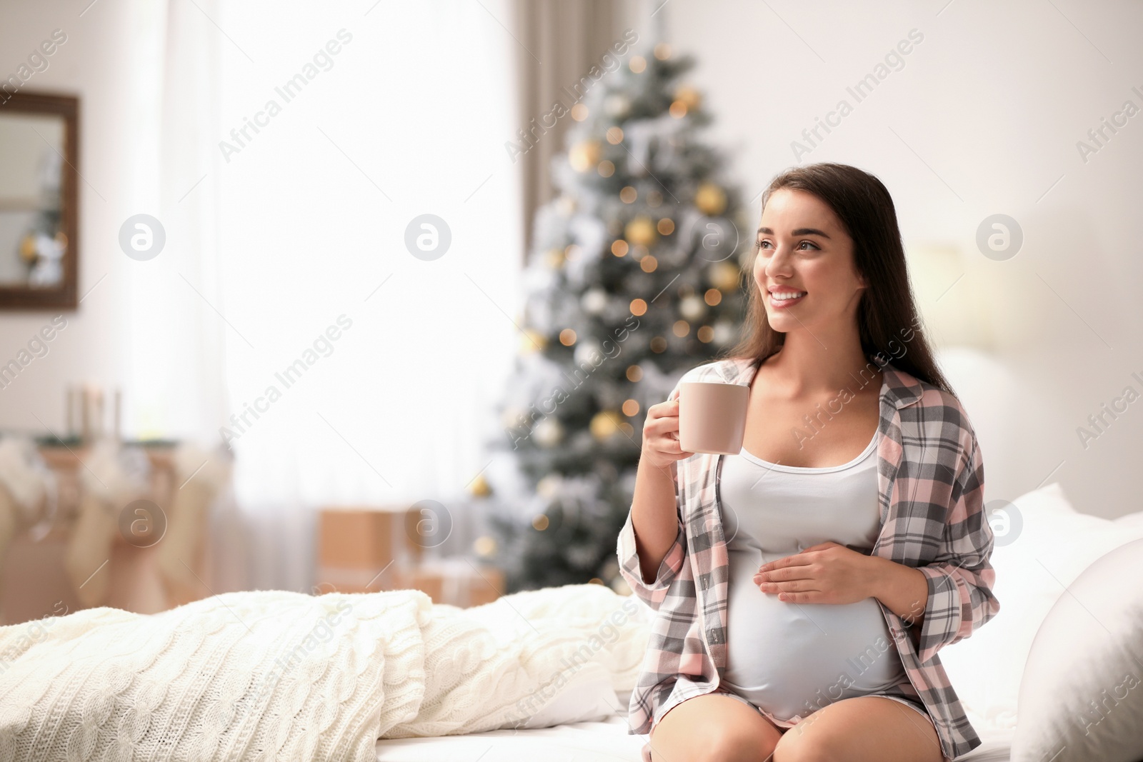 Photo of Happy pregnant woman on bed in room decorated for Christmas. Expecting baby