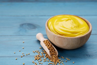 Sauce bowl with delicious mustard and seeds on light blue wooden table, closeup. Space for text