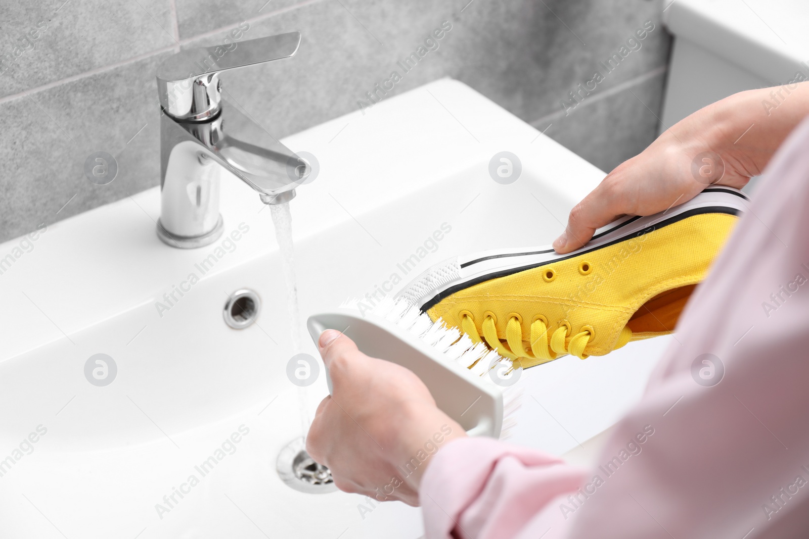 Photo of Woman washing stylish sneakers with brush in sink, closeup