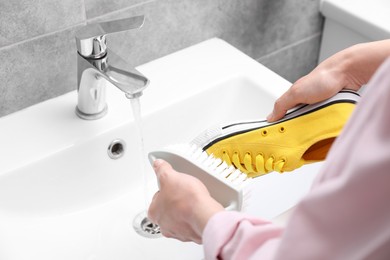 Photo of Woman washing stylish sneakers with brush in sink, closeup