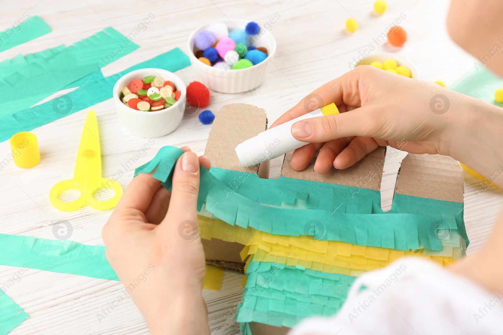 Photo of Woman decorating cardboard cactus at white wooden table, closeup. Pinata DIY