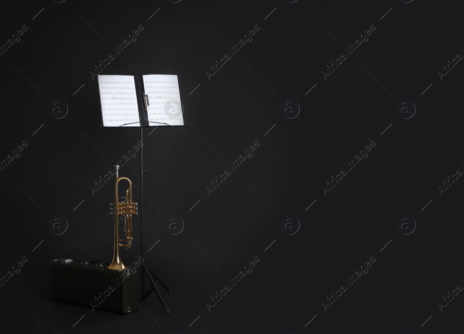 Photo of Trumpet, case and note stand with music sheets on black background. Space for text