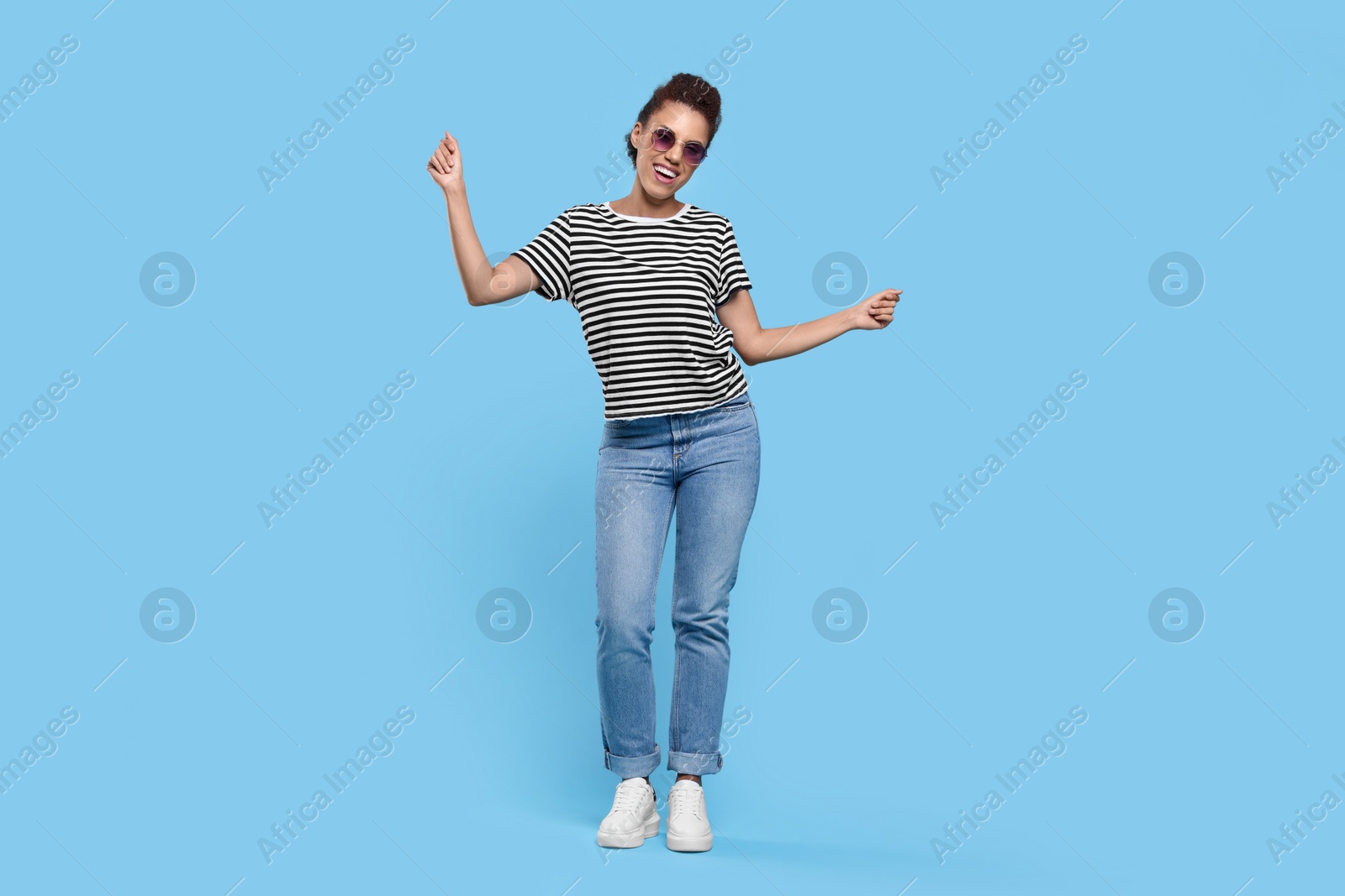 Photo of Happy young woman in stylish sunglasses dancing on light blue background