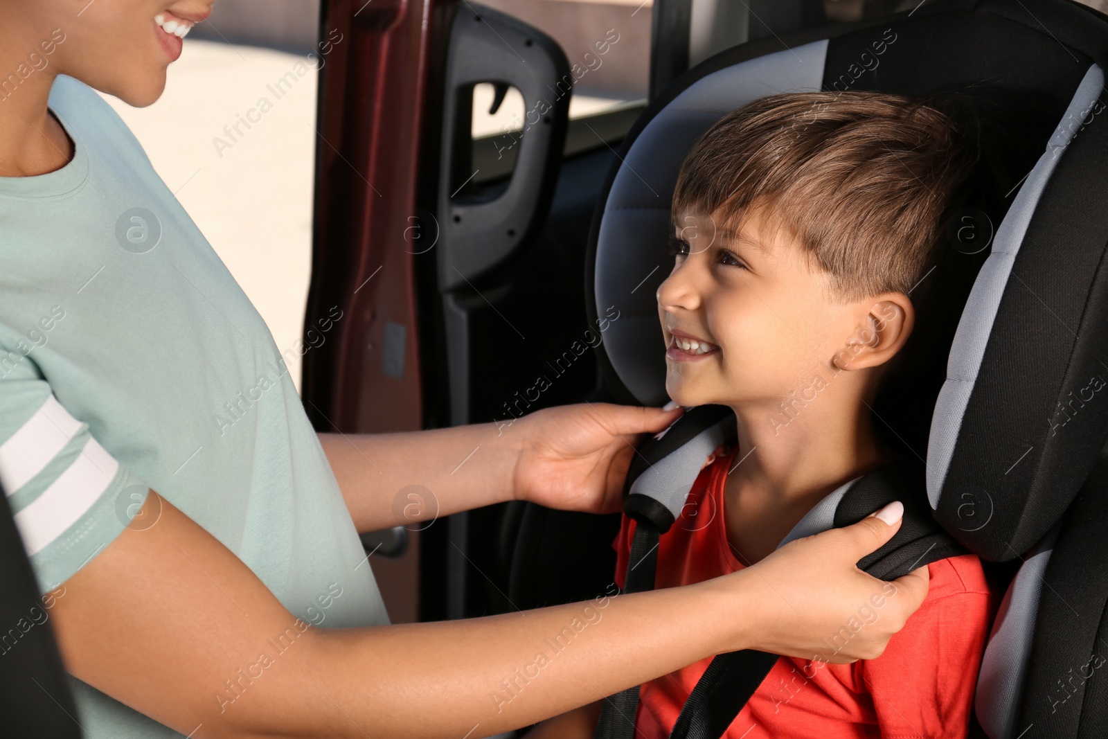 Photo of Mother fastening her son with car safety belt in child seat