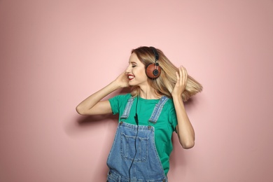 Beautiful young woman with healthy long blonde hair and headphones on color background