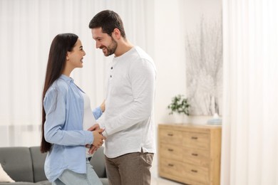 Happy pregnant woman with her husband at home, space for text
