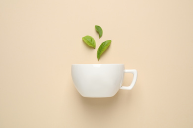 Photo of Fresh tea leaves and cup on beige background, top view