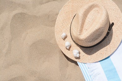 Photo of Straw hat with seashells and beach towel on sand, top view. Space for text