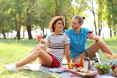 Photo of Happy couple with glasses of wine sitting on lawn. Summer picnic