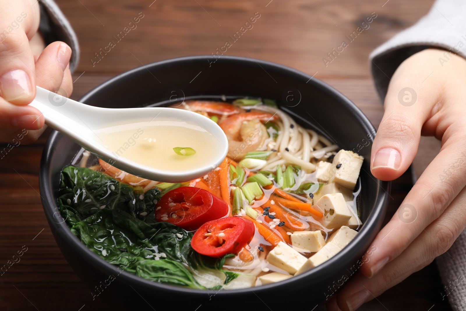 Photo of Woman eating delicious ramen with spoon at table, closeup. Noodle soup