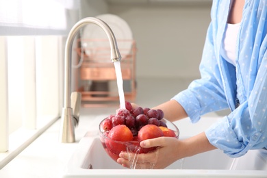 Photo of Woman washing fresh grapes and nectarines in kitchen sink, closeup