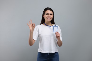Photo of Smiling woman holding vip pass badge and showing ok gesture on grey background